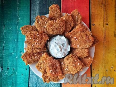 Куриные наггетсы, запечённые в панировочных сухарях, достать из духовки, переложить&nbsp;на блюдо и подать к столу, дополнив любимым соусом.