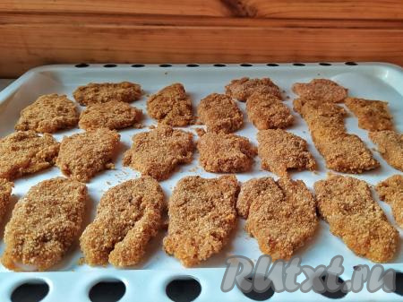 Выложить запанированное филе на противень (у меня размер противня 30 см х 40 см), застеленный пергаментом.&nbsp;Запекать куриные наггетсы в разогретой духовке при температуре 200 градусов 20 минут. Затем вынуть противень, перевернуть каждый наггетс и отправить в духовку ещё на 20 минут.