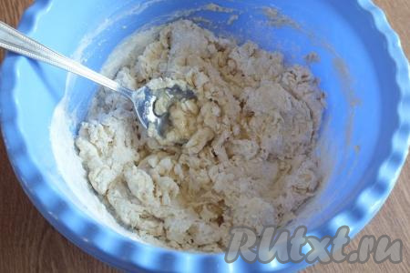 Всыпьте муку, добавьте растительное масло и начните перемешивать ложкой. Тесто медленно будет собираться в комочки. Как только начнёт отставать от краёв миски, продолжайте выполнять замес руками.