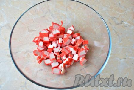 Возьмите глубокую чашу, чтобы в ней было удобно смешивать все составляющие салата. Крабовые палочки, если они заморожены, оставьте при комнатной температуре до полного размораживания, затем освободите их от упаковки и нарежьте на кубики. Переложите нарезанные палочки в чашу.