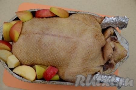 Поместить нафаршированную утку в утятницу, с боков утятницы расположить оставшиеся кусочки яблок. Ножки утки можно обернуть фольгой.