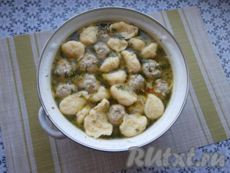 Дать супу закипеть, а после этого варить на слабом огне 5-7 минут. Фрикадельки должны всплыть на поверхность супа. Теперь чайную ложку на несколько секунд поместить в суп, а затем набирать в эту ложку&nbsp;тесто для галушек и опускать в кипящий суп. Дать супу снова закипеть, добавить измельчённый укроп и проварить на небольшом огне минут 5-6.