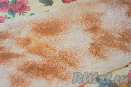 С помощью кондитерской кисти смазываем тесто взбитым яйцом, присыпаем сахаром и корицей (у меня слоёное тесто было в виде одного пласта, поэтому я его раскатала и у меня получился большой прямоугольник. Если же у вас тесто в виде двух пластов, тогда раскатайте по очереди каждый пласт, а затем равномерно распределите сахар и корицу по двум раскатанным прямоугольникам).
