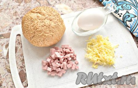 Булочка необязательно должна быть свежей, подойдёт хлебобулочное изделие уже «залежавшееся». Сразу включаем духовку и выставляем температурный режим на 180 градусов. Колбасу нарезаем на мелкие кубики. Сыр натираем на тёрке.