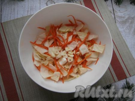 Посолить капусту с морковкой, немного помять руками, затем добавить зубчики чеснока, нарезанные на пластины.