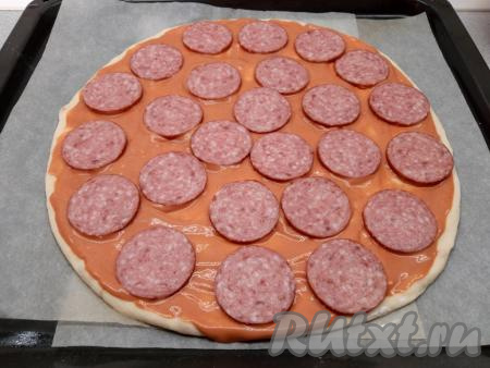 Кетчуп смешиваю с майонезом. Щедрым слоем наношу половину смеси кетчупа и майонеза на пиццу, выкладываю половину кусочков колбасы.