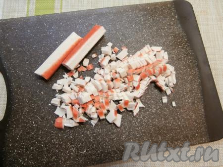 Прежде всего нужно отварить до готовности рис, для этого после промывания его нужно выложить в кастрюлю, залить холодной водой (воды должно быть в 2 раза больше, чем риса), поставить на огонь, а после закипания воду подсолить, перемешать рис и отварить его на небольшом огне до готовности (минут 15), помешивая. Вода полностью должна испариться, остудить отваренный рис. Замороженные крабовые палочки полностью разморозить, а затем освободить их от плёнки и нарезать на небольшие кусочки.