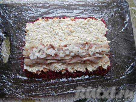 Из филе сельди удалить косточки, затем нарезать на тонкие кусочки. Очистить половину луковицы и мелко нарезать. Ближе к одному длинному краю прямоугольника выложить нарезанную тонкими кусочками селёдку, сверху на селёдке разместить лук (как на фото).