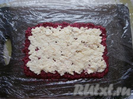 На доску выложить пищевую плёнку, сложенную в два слоя. На ней разместить свеклу, придав ей вид прямоугольника. Сверху свеклы, отступив от краёв свеклы по 1-1,5 сантиметра, выложить слой картофеля.