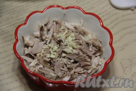 Разобрать куриное мясо, отделив мякоть от костей. Порвать мясо на волокна и разложить равномерно по формам. Чеснок почистить и мелко порубить. Добавить чеснок в формы с мясом.