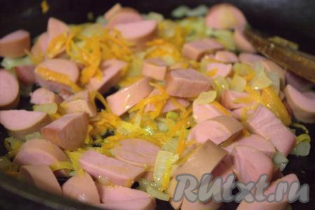 Очистить от плёнки, произвольно нарезать сосиски и добавить в сковороду к обжаренным овощам. Обжаривать сосиски с луком и морковью, помешивая, 5-7 минут.