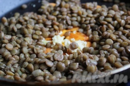 Добавьте к моркови сваренную чечевицу, мелко порубленный или пропущенный через пресс чеснок, перемешайте, уменьшите огонь до минимума и немного потомите всё вместе.