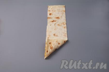 Заверните уголок лаваша на начинку так, чтобы получился треугольник.