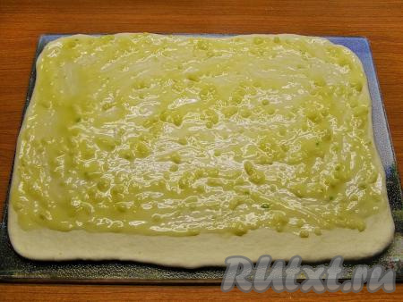 Тесто разминаем руками и раскатываем его в форме прямоугольника размером, примерно, 25 см на 35 см и толщиной около 0,7-1 см. Смазываем тесто смесью сливочного масла и чеснока, не доходя до нижнего длинного края, примерно, 2 см.