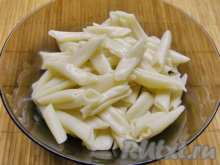 Макароны выкладываем в кастрюлю с кипящей чуть подсоленной водой, даём закипеть, а затем на умеренном огне отвариваем до готовности (на это потребуется минут 7-8 после закипания, более точно время варки можно посмотреть в инструкции на упаковке макаронных изделий, которые вы варите). Затем воду сливаем через дуршлаг, в макароны добавляем 1 столовую ложку растительного масла, перемешиваем и оставляем немного остыть.