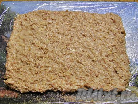 Доску (или стол) застилаем пищевой плёнкой и выкладываем на неё фарш. Разравниваем его руками, придавая форму прямоугольника размером, примерно, 17 сантиметров на 25 сантиметров и толщиной около 1,5 сантиметров.