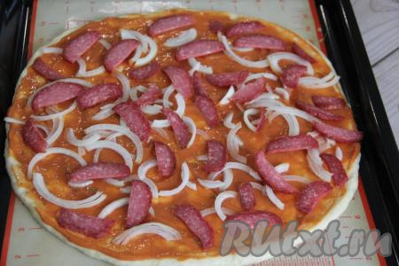 Выложить лук и колбасу на смазанную творожную основу пиццы.&nbsp;