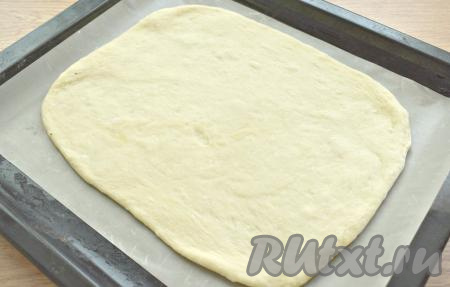 Поднявшееся тесто обминаем (вес теста у меня получился 500 грамм), делим на 2 неравных куска (один кусок должен быть, примерно, весом 300 грамм, а другой - 200 грамм). Большую часть теста раскатываем на припылённой мукой поверхности в овальный (или круглый) пласт толщиной около 7 миллиметров. Это будет основание пирога. Перекладываем его сразу на противень, который лучше застелить пергаментом (или специальным листом для выпечки).