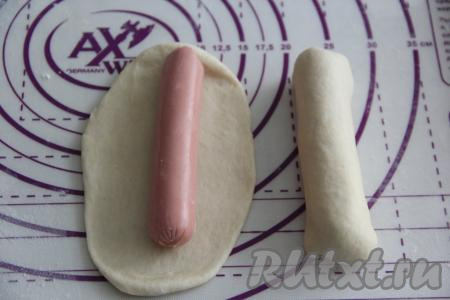 Обмять тесто и разделить на 15 частей. Сосиски очистить от плёнки. Каждую часть теста на припылённой мукой поверхности раскатать в овал, длина которого должна быть чуть больше длины сосиски. Выложить в центр каждого овала сосиску.