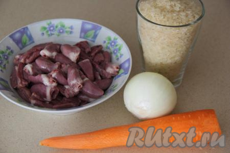 Подготовить продукты для приготовления плова с куриными сердечками на сковороде. Разрезать сердечки пополам и хорошо промыть их от сгустков крови. Луковицу, зубчики чеснока и морковку почистить. Рис промыть, лишнюю воду с промытой крупы слить.