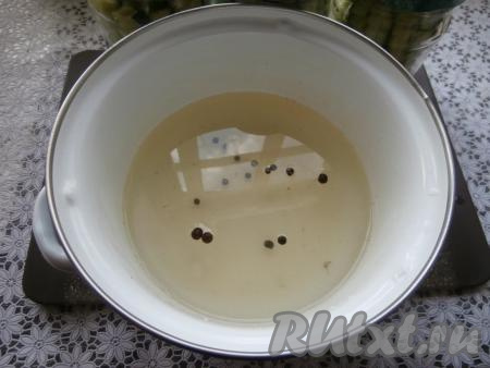 По прошествии 10 минут воду из баночек аккуратно слить в кастрюлю, снова воду вскипятить и залить огурцы второй раз. Оставить банки, прикрыв крышками, на 4-5 минут. Затем слить воду снова в кастрюлю, добавить соль, сахар, горошинки душистого и чёрного перцев, поставить на огонь.
