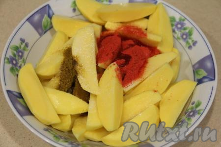 Нарезать картошку на крыпные дольки, переложить в глубокую миску, добавить соль, хмели-сунели и паприку, влить масло.