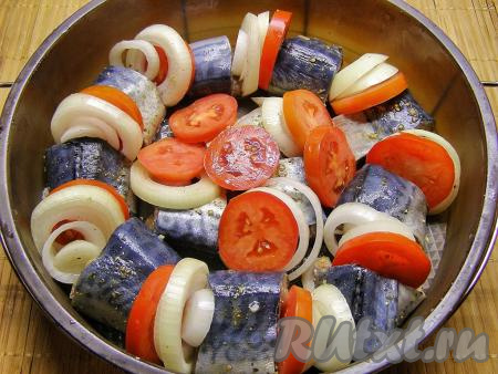 В форму для запекания выкладываем кусочки скумбрии. Я использовала силиконовую форму диаметром 24 сантиметра. Если у вас форма не из силикона или без антипригарного покрытия, тогда её нужно предварительно немного смазать растительным маслом, чтобы рыбка и овощи не прилипли в процессе запекания ко дну и стенкам посуды. Между кусочками рыбы кладём кольца лука и кружочки помидоров. Несколько кружочков помидоров и колец лука я выложила поверх скумбрии.
