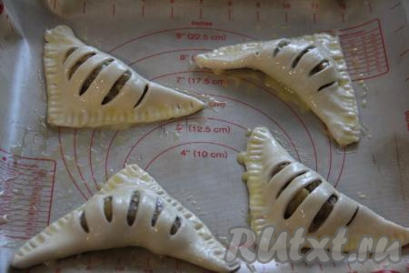 Переложить заготовки слоек с бананами на противень, застеленный ковриком для выпечки (или пергаментом). Чтобы выпечка получилась румяной, смазать верх заготовок желтком, предварительно взбитым вилкой.