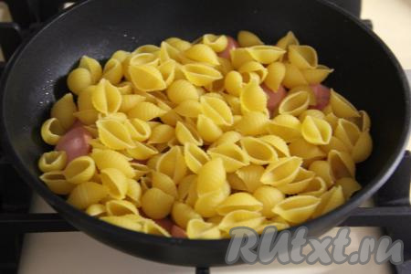 В сковороду с обжаренными сосискам всыпать сухие макароны.