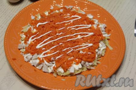 Морковку почистить и сразу вырезать из неё носик, щёчки и ротик снеговика. Оставшуюся морковку натереть на крупной тёрке и равномерно разложить поверх курицы, нанести немного майонеза.
