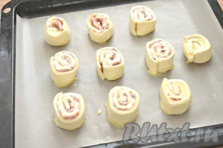 Заготовки слоек перекладываем разрезом вверх на противень, застеленный листом для выпечки (или пергаментом). Выкладывать рулетики нужно на расстоянии друг от друга, так как они увеличатся в размере во время выпечки. Бока и верхушку рулетиков смазываем взбитым яйцом.