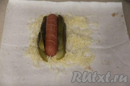 Огурцы нарезать на тонкие полоски (или длинные брусочки). Выложить сосиску на сыр. С двух сторон от сосиски расположить несколько полосок огурчика.