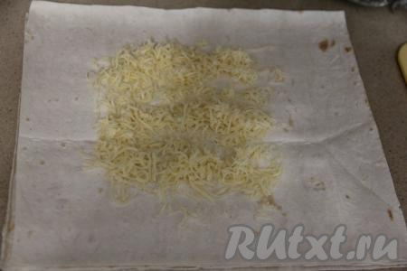 Взять одну отрезанную часть лаваша, на середину выложить часть сыра, натёртого на мелкой тёрке.