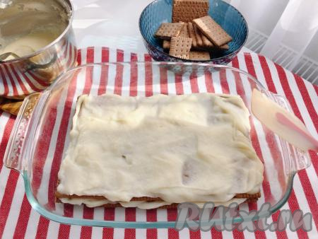 При помощи силиконовой лопатки равномерно распределяем крем. Затем выкладываем второй слой печенья, сверху равномерно наносим ещё треть крема. И повторяем эту процедуру ещё раз. В общей сложности у нас должно получиться три слоя печенья и три слоя заварного крема.