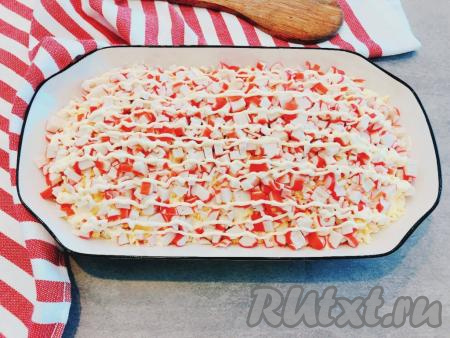 Третьим слоем выкладываем крабовые палочки, наносим сеточку из майонеза.