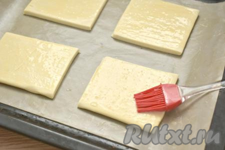 Заранее тесто достаём из морозилки, оставляем разморозиться при комнатной температуре. У меня слоёное тесто разморозилось через 1 час. Вначале первый пласт теста, не раскатывая, разрезаем на 4 квадрата и сразу перекладываем на противень, застеленный ковриком для выпечки (или пергаментом). Яйцо в небольшой ёмкости взбиваем вилкой. Смазываем квадраты из теста взбитым яйцом.