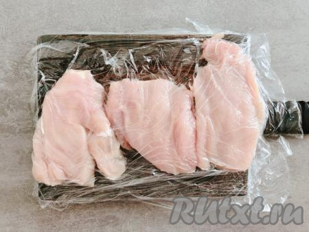 Накрываем нарезанные кусочки филе пищевой плёнкой или полиэтиленовым пакетом (я накрыла ещё и доску, так как она у меня деревянная). Каждый кусочек мяса слегка отбиваем с одной стороны молоточком для отбивных. Старайтесь, чтобы все кусочки получились примерно одинаковой толщины (примерно 1 сантиметр).