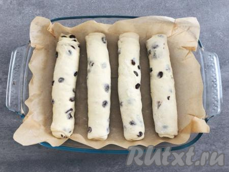 Получившийся пласт скатываем в рулет, начиная с широкой стороны, и выкладываем в форму для запекания, предварительно застеленную пергаментом (или смазанную растительным маслом). Таким же образом формируем рулеты из 3 оставшихся частей теста и выкладываем их в форму на небольшом расстоянии друг от друга. Накрываем форму с рулетами полотенцем и оставляем в тепле подниматься ещё на 20 минут.