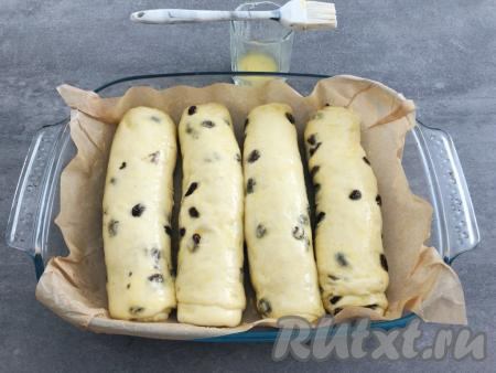 В это время в небольшой посуде смешиваем яичный желток с 2 чайными ложками молока, перемешиваем. По истечении 20 минут округлившиеся булочки с изюмом при помощи силиконовой кисти смазываем яично-молочной смесью (благодаря смазыванию, на булочках в процессе выпечки получится румяная корочка).