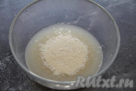 Изюм промыть водой, затем залить кипятком на 4-5 минут, после этого воду слить, а изюм обсушить на полотенце (или на салфетках). В глубокую миску влить тёплую воду. Температура воды должна быть не выше 40 градусов. Всыпать сухие дрожжи и сахар, перемешать и оставить на 15 минут.