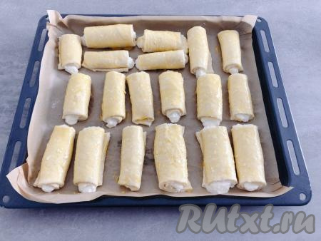 Обрезки теста не выбрасываем, а собираем в комок и, повторно раскатывая, формируем булочки. Всего у меня получилось 19 булочек-рулетиков. Сформированные творожные булочки перекладываем на противень, застеленный пергаментной бумагой (или смазанный растительным маслом). В небольшую ёмкость разбиваем яйцо, отделяем желток, добавляем в него 2 чайных ложки молока и перемешиваем до однородности. С помощью силиконовой кисточки смазываем поверхность булочек яично-молочной смесью.