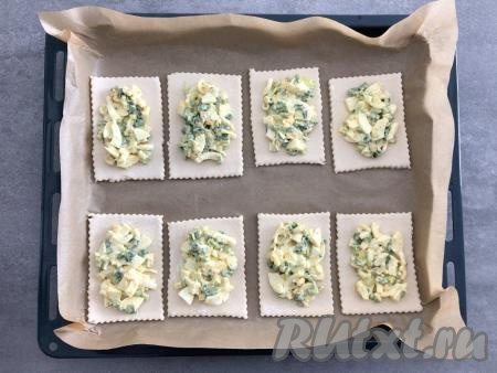 Получившиеся прямоугольники из слоёного теста переложить на противень, застеленный пергаментной бумагой. В центр каждого прямоугольника выложить примерно столовую ложку начинки, оставляя края свободными.