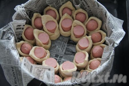 Круглую форму для выпечки (у меня форма диаметром 28 сантиметров) застелить пергаментом для выпечки и смазать маслом. Выложить сосиски в тесте по кругу в два ряда.