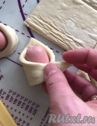 Обернуть каждый кусочек сосиски в треугольник из слоёного теста, как на фото, острые углы треугольника будут внахлёст, хорошо закрепляем пальцами место соединения уголков.