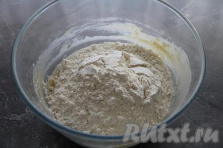 Постепенно начать всыпать просеянную муку, сначала перемешивая тесто для бубликов столовой ложкой. А затем, добавляя частями муку, вымесить тесто руками в течение 5-7 минут.