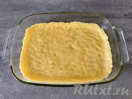 Форму для выпечки (я взяла форму размером 25 на 35 сантиметров) слегка смазываем растительным маслом. Достаём тесто из холодильника, равномерно распределяем по дну формы, формируем бортики высотой примерно 1 сантиметр, при помощи вилки делаем проколы в тесте (благодаря проколам песочное тесто не будет вздуваться при выпечке).