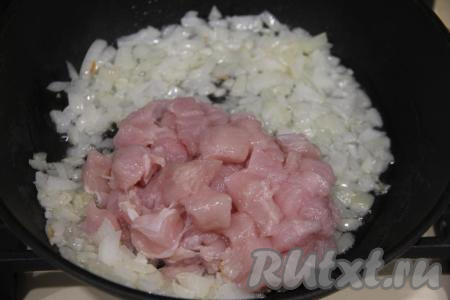 В растительное масло, разогретое на сковороде, выложить лук и обжарить его на среднем огне в течение 3 минут, иногда помешивая, затем добавить кусочки куриного мяса, перемешать.