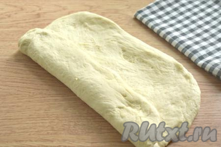 Затем тесто растягиваем (или раскатываем) на столе, присыпанном мукой в не тонкий прямоугольник. Сворачиваем прямоугольный пласт теста в рулет.