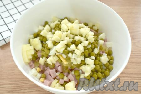 Очищаем от кожуры и семечек яблоко, нарезаем его на маленькие кубики и тоже выкладываем в миску с салатом "Оливье".