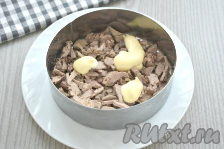 Теперь можно приступать к формированию салата слоями. Салат можно выкладывать в один большой салатник. Я готовила салат порционно, раскладывая ингредиенты по 2 сервировочным кольцам диаметром 11 сантиметров. Ставим сервировочное кольцо на плоскую тарелку. На дно одной формы выкладываем половину куриной печени, нарезанной на небольшие кубики (или соломкой). Во второе кольцо выкладываем вторую половину нарезанной печёнки. Слой из печени смазываем майонезом.